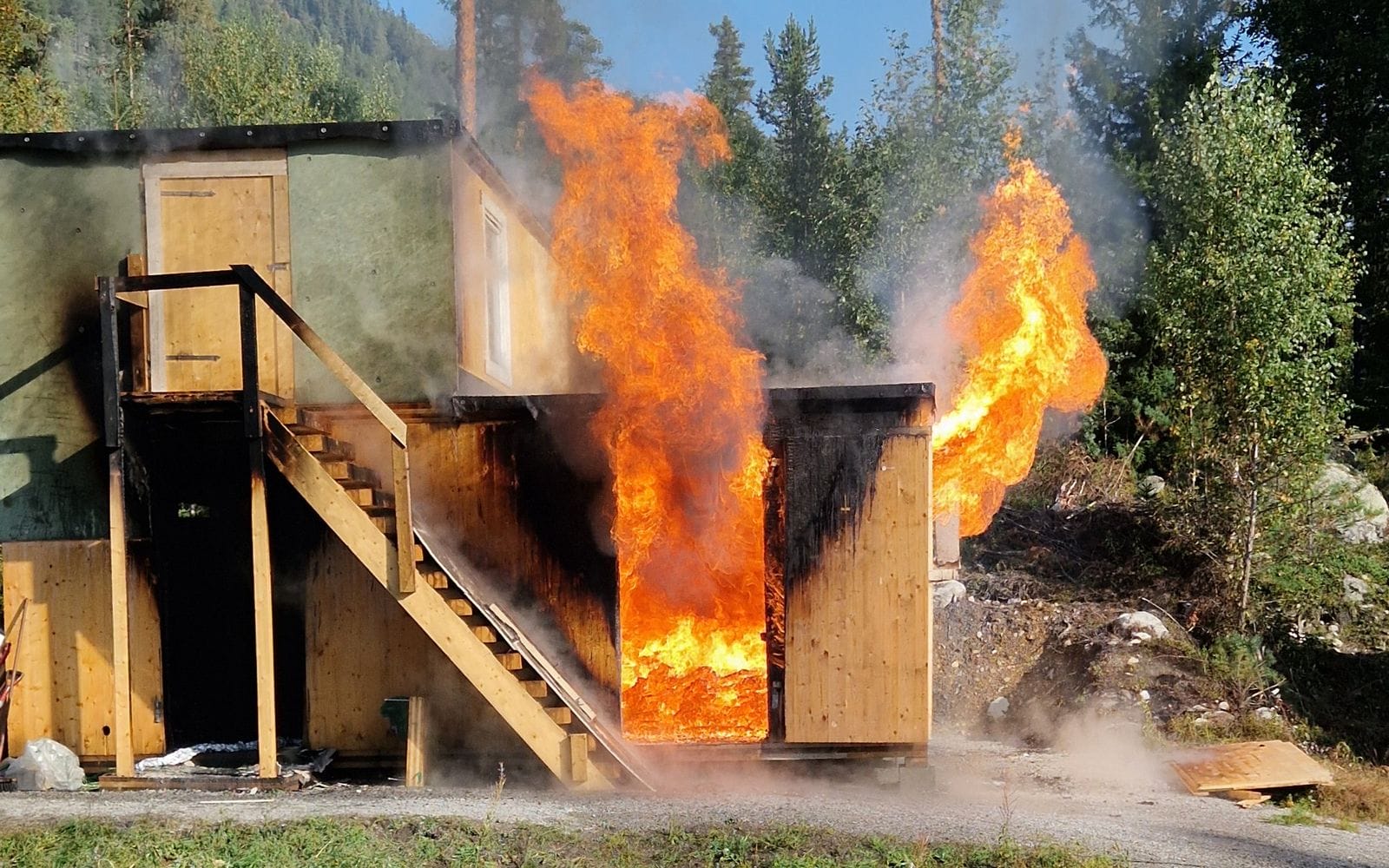 Fullskala branntest av massivtrebygg med flammer ut av døren og vinduet på Torpomoen